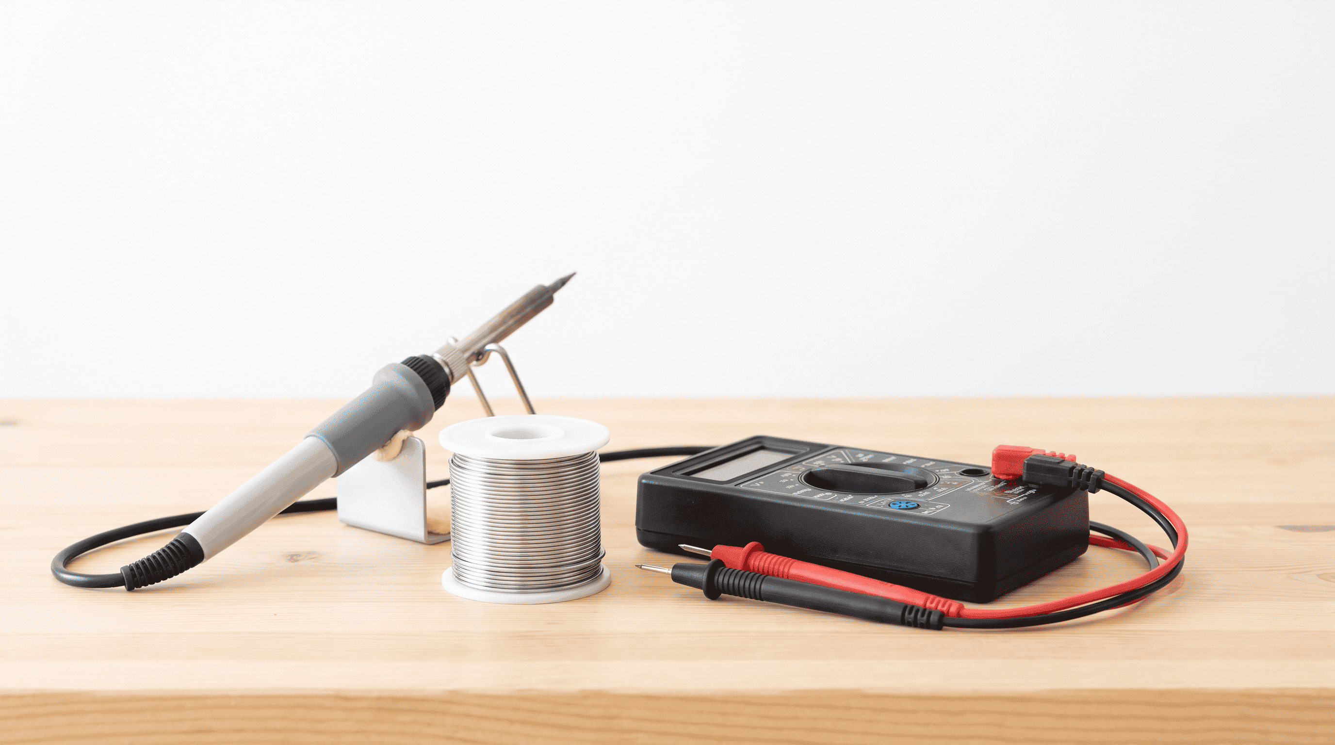 Soldering iron, solder spool and digital multimeter arranged on a light bench