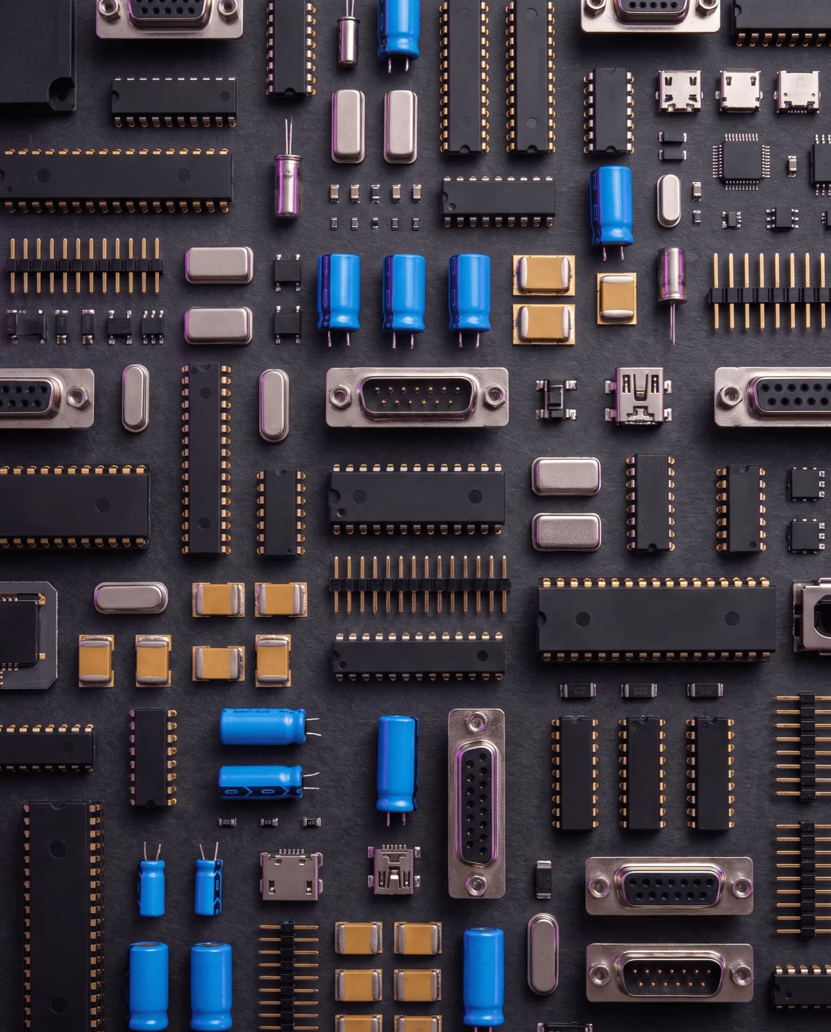 Assorted electronic components including ICs, connectors, and capacitors on a dark surface